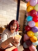 Jesz proost lachend met een kopje koffie naast een ballonnenpilaar in het nieuwe pand